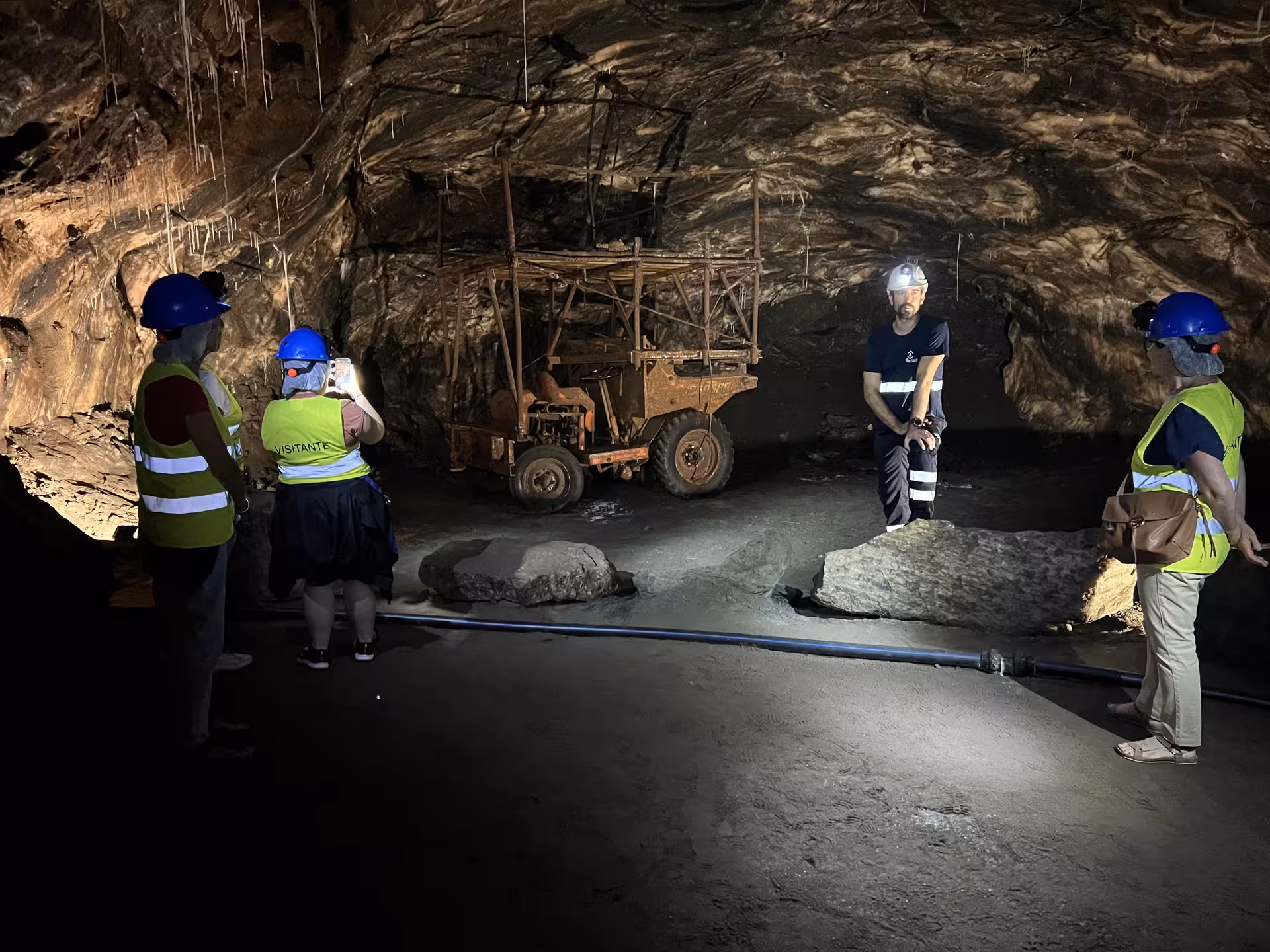 Tour group explores Loulé's rock salt mine with a guide, surrounded by mining equipment and illuminated cave walls.