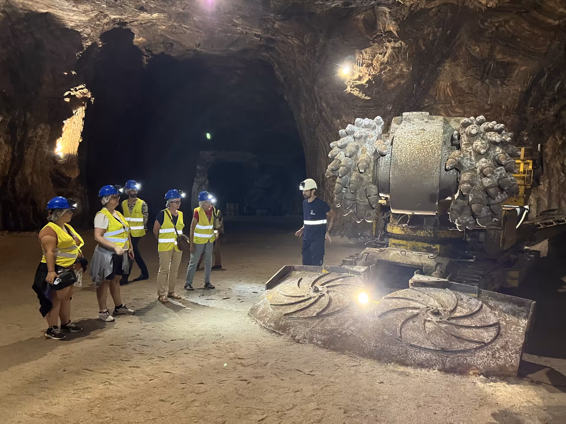 Visitors in safety gear learn about mining machinery inside Loulé's rock salt mine, highlighting underground exploration.