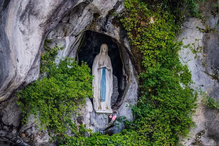 Statue of Virgin Mary in the Grotto of Lourdes, surrounded by lush greenery, a key site on the city walking tour.