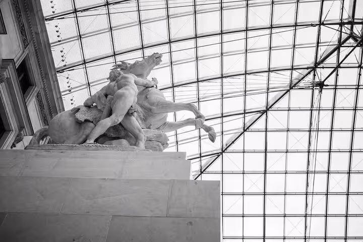 Dramatic sculpture under the Louvre's iconic glass roof, highlighting the grandeur of the museum tour experience.
