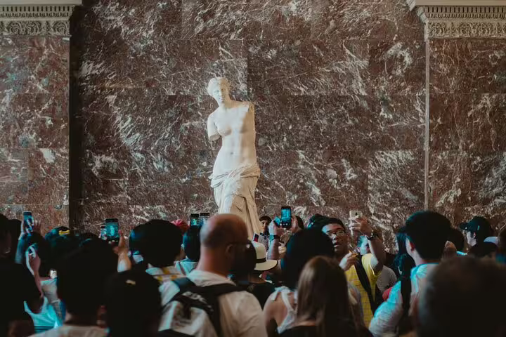 Crowd gathered around the Venus de Milo at the Louvre Museum, capturing the excitement of a Mona Lisa tour visit.