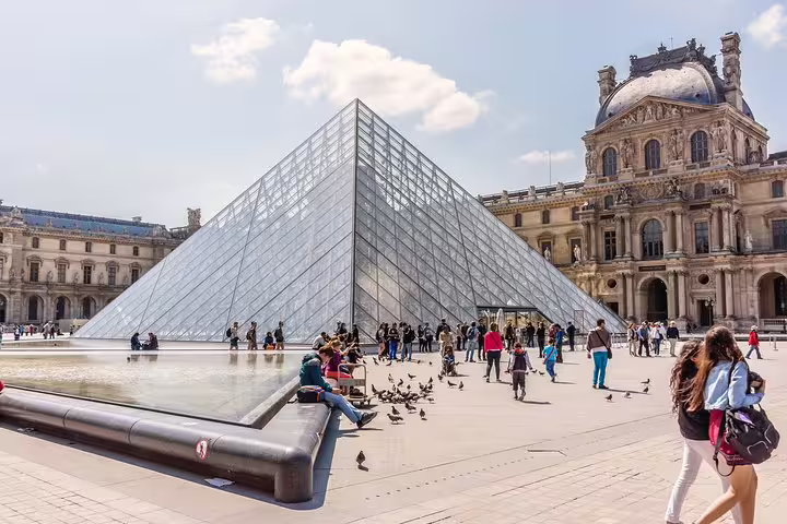 Visitors gather around the iconic Louvre Pyramid in Paris, enjoying a sunny day as part of the Highlights & Secrets of Paris tour.