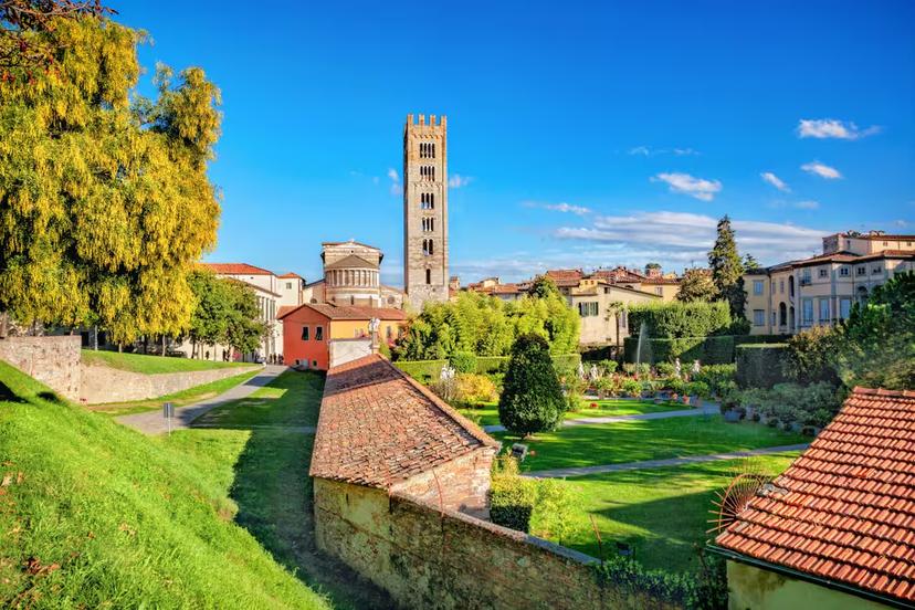 Scenic view of Lucca's historic architecture and lush gardens under a clear blue sky, showcasing Tuscany's charm.