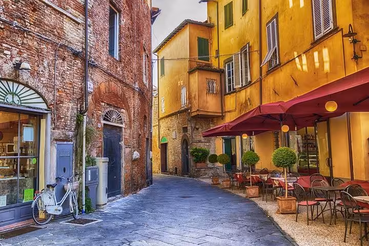 Charming street view in Lucca with colorful buildings, outdoor café, and bicycle, perfect for a Livorno port excursion.