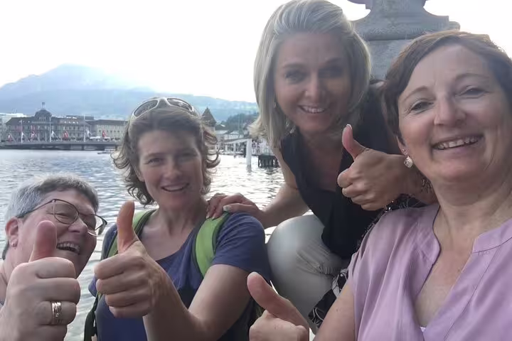 Group selfie with thumbs up by Lake Lucerne waterfront, celebrating a self-guided scavenger hunt tour