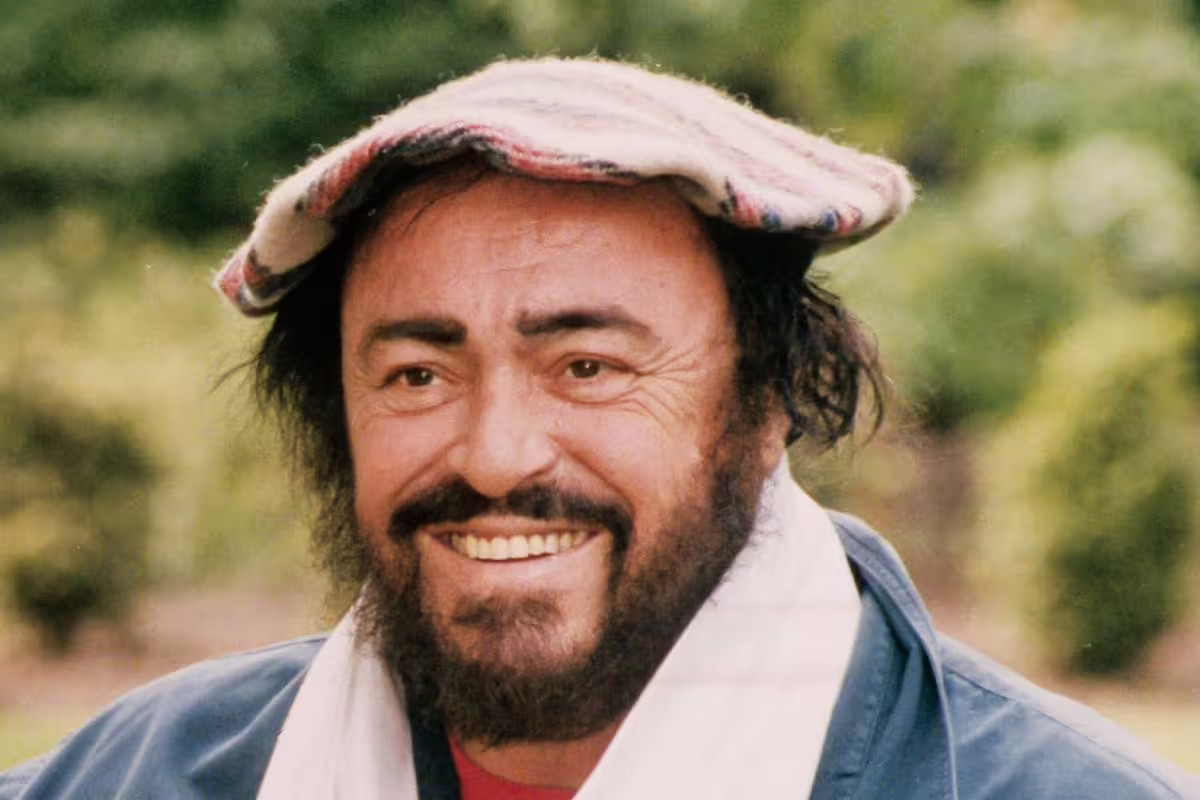 Luciano Pavarotti smiling outdoors in a flat cap, image shown on the Modena Pavarotti House Museum tour