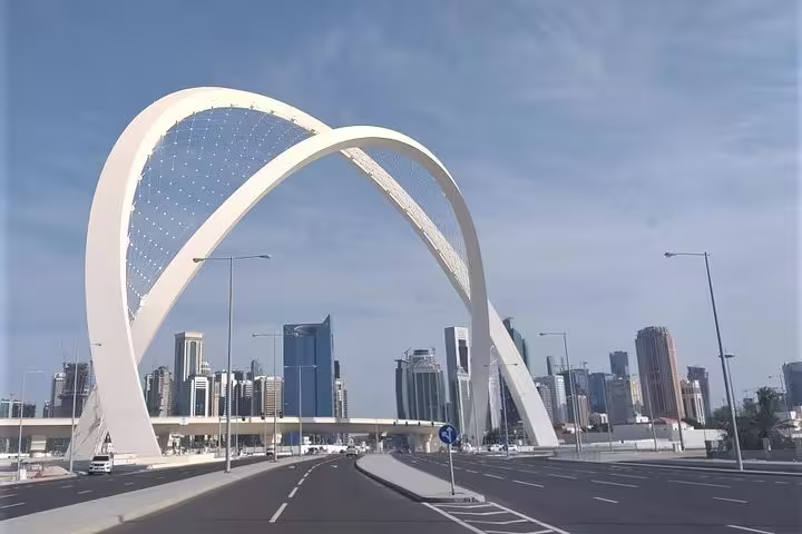 Stunning view of the iconic arches of Lusail Bridge in Doha, with the city skyline under a clear blue sky.