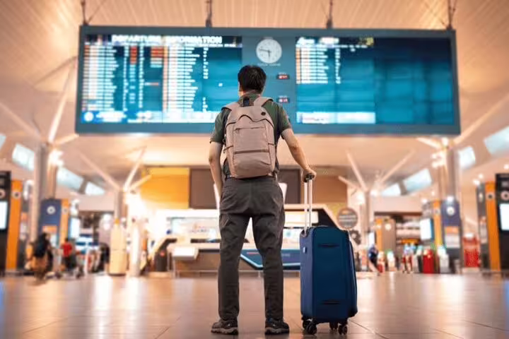 Traveler with suitcase under departures board booking Luxor Airport private transfer service for fast, secure pickup