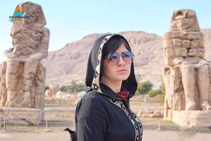 Traveler at Luxor Colossi of Memnon on Nile West Bank tour, with desert hills behind in Egypt