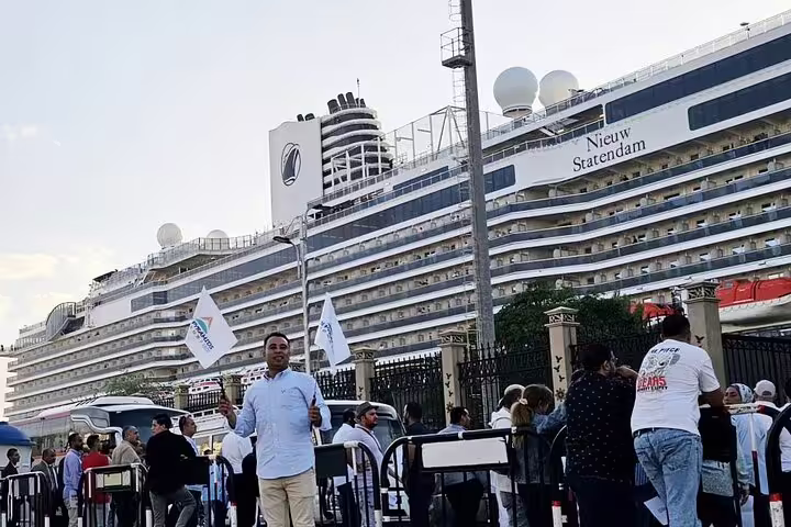 Cruise passengers meet tour staff at Safaga Port for Luxor day trip, with ship in background and flags