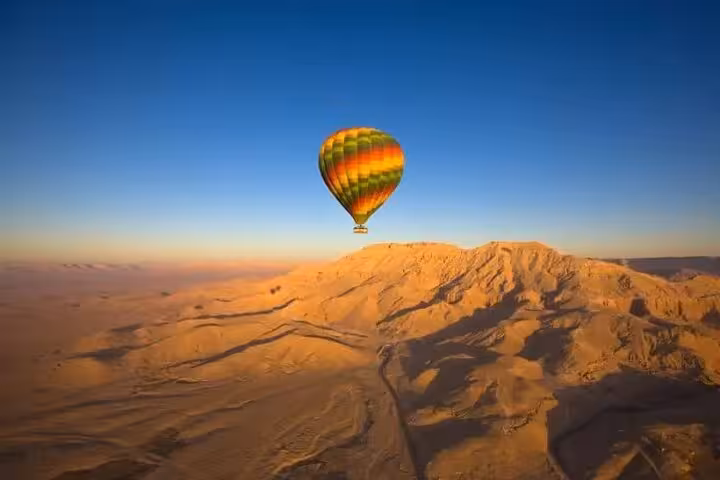 Colorful hot air balloon floating above Luxor desert hills at sunrise, scenic Egypt balloon tour view