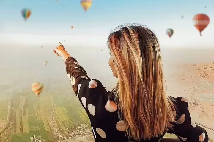 Traveler pointing at hot air balloons over Luxor at sunrise, scenic Nile Valley flight experience in Egypt