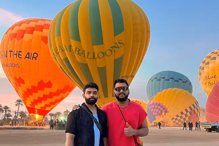 Guests posing at Luxor hot air balloon launch field at sunrise before West Bank flight with hotel pickup and drop-off