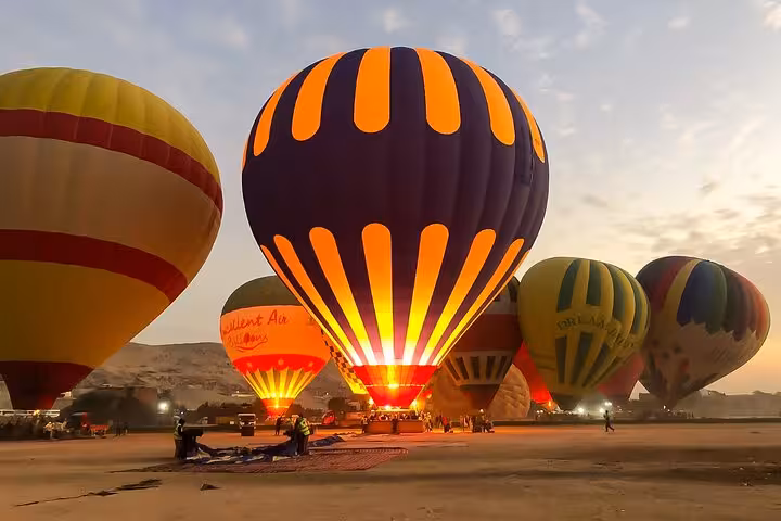Luxor hot air balloon launch at dawn with glowing burners, Egypt sunrise flight with transfers included