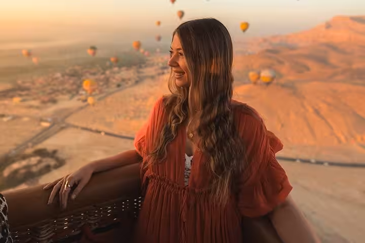 Traveler in Luxor hot air balloon basket at sunrise, floating over the Nile Valley on a guided tour with transfers