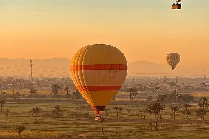 Single hot air balloon drifting over Luxor fields at sunrise, Luxor balloon ride with hotel pickup included