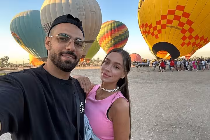 Couple selfie at Luxor hot air balloon launch site, colorful balloons ready for Nile River Valley sunrise flight