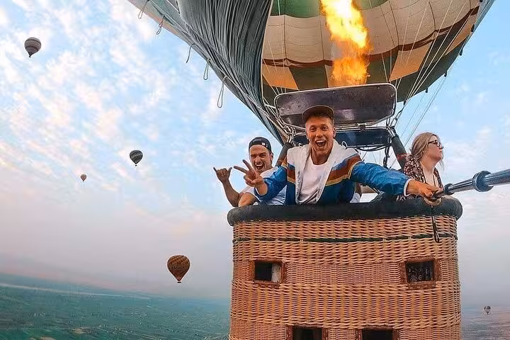 Happy travelers in basket during Luxor hot air balloon ride over Nile River Valley at sunrise, Egypt