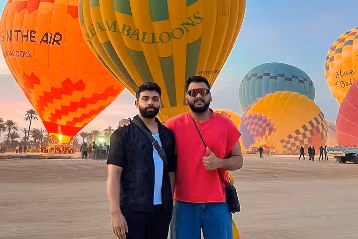 Travelers posing beside inflated balloons at Luxor sunrise hot air balloon ride launch site with hotel transfers