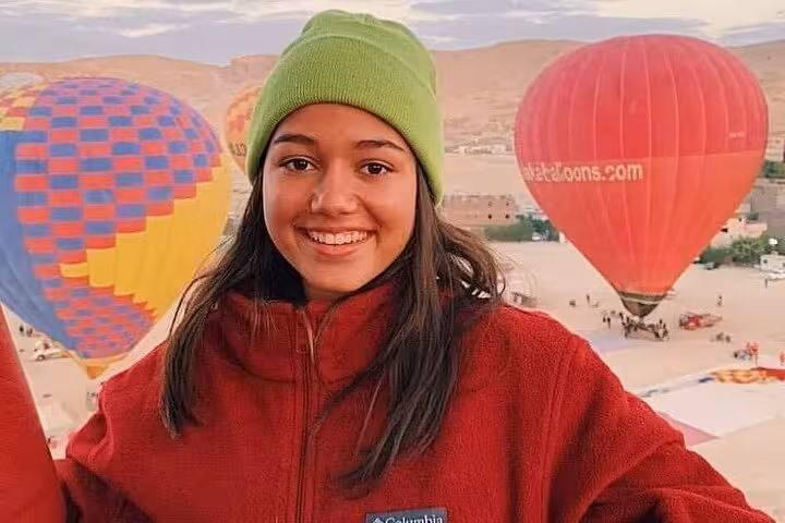 Smiling guest in warm jacket before Luxor hot air balloon tour with colorful balloons over Nile Valley desert