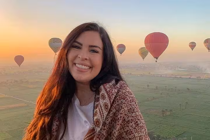 Smiling traveler in hot air balloon over Luxor at sunrise, floating above Nile River Valley farmlands