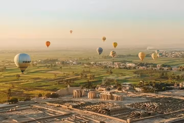 Hot air balloons floating over Luxor temples and green Nile River Valley fields on sunrise balloon tour