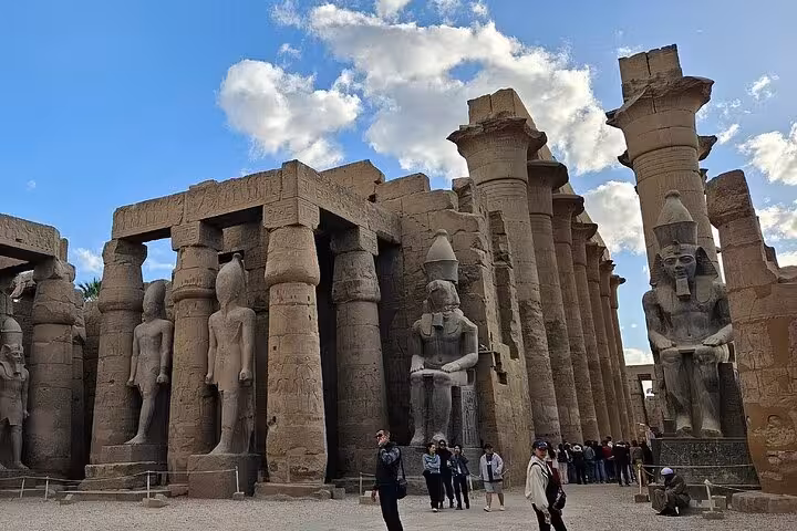 Visitors explore the grand statues and columns of the ancient Luxor Temple under a clear blue sky.