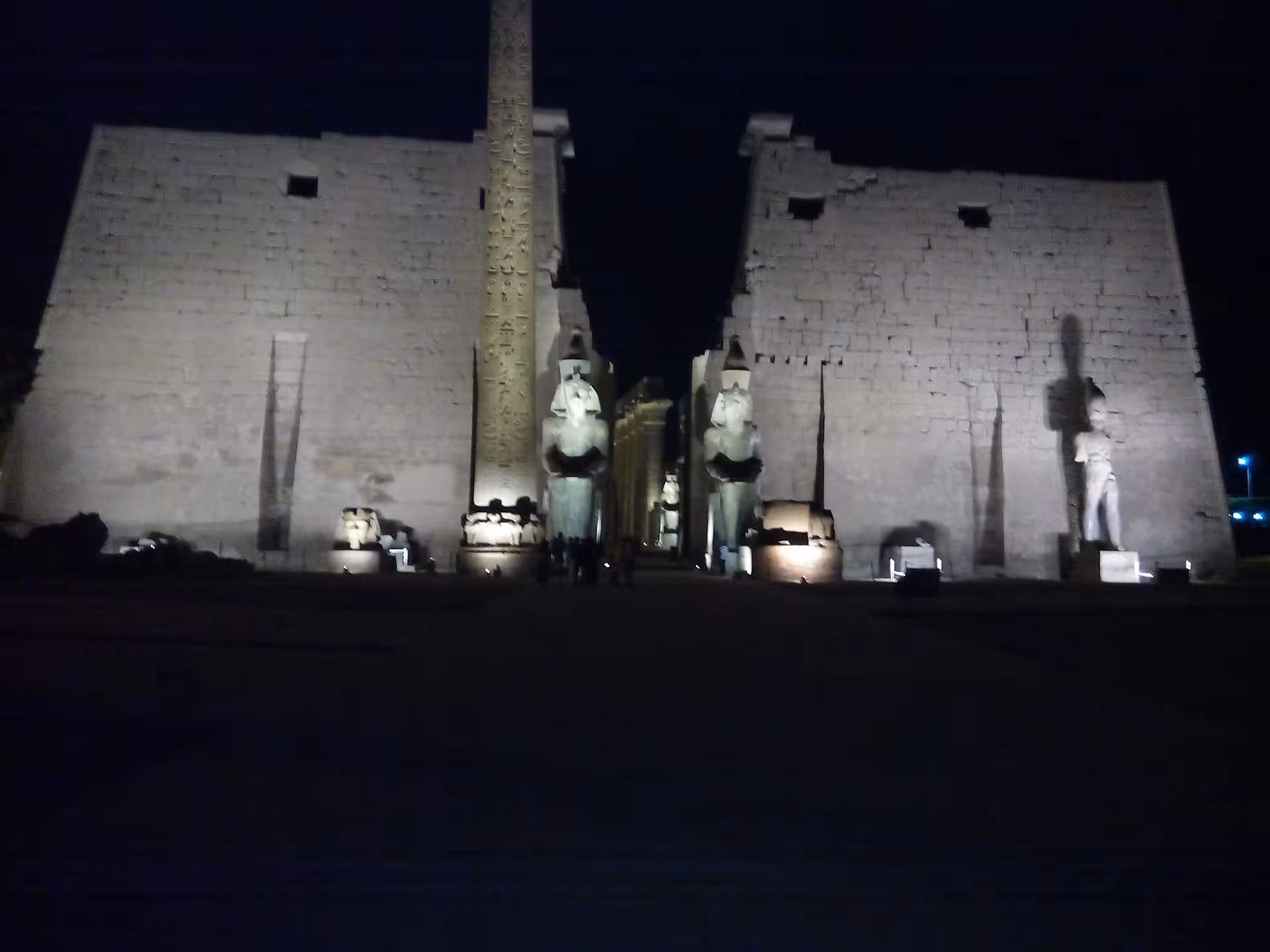 Luxor Temple's grand entrance illuminated at night, featuring colossal statues and ancient hieroglyphics.