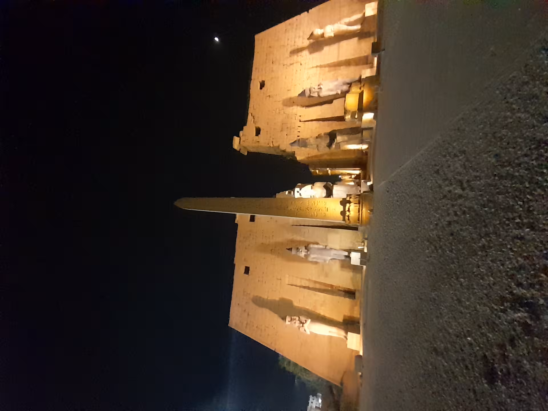 Illuminated Luxor Temple at night showcasing majestic ancient Egyptian statues and towering obelisk under a starry sky.