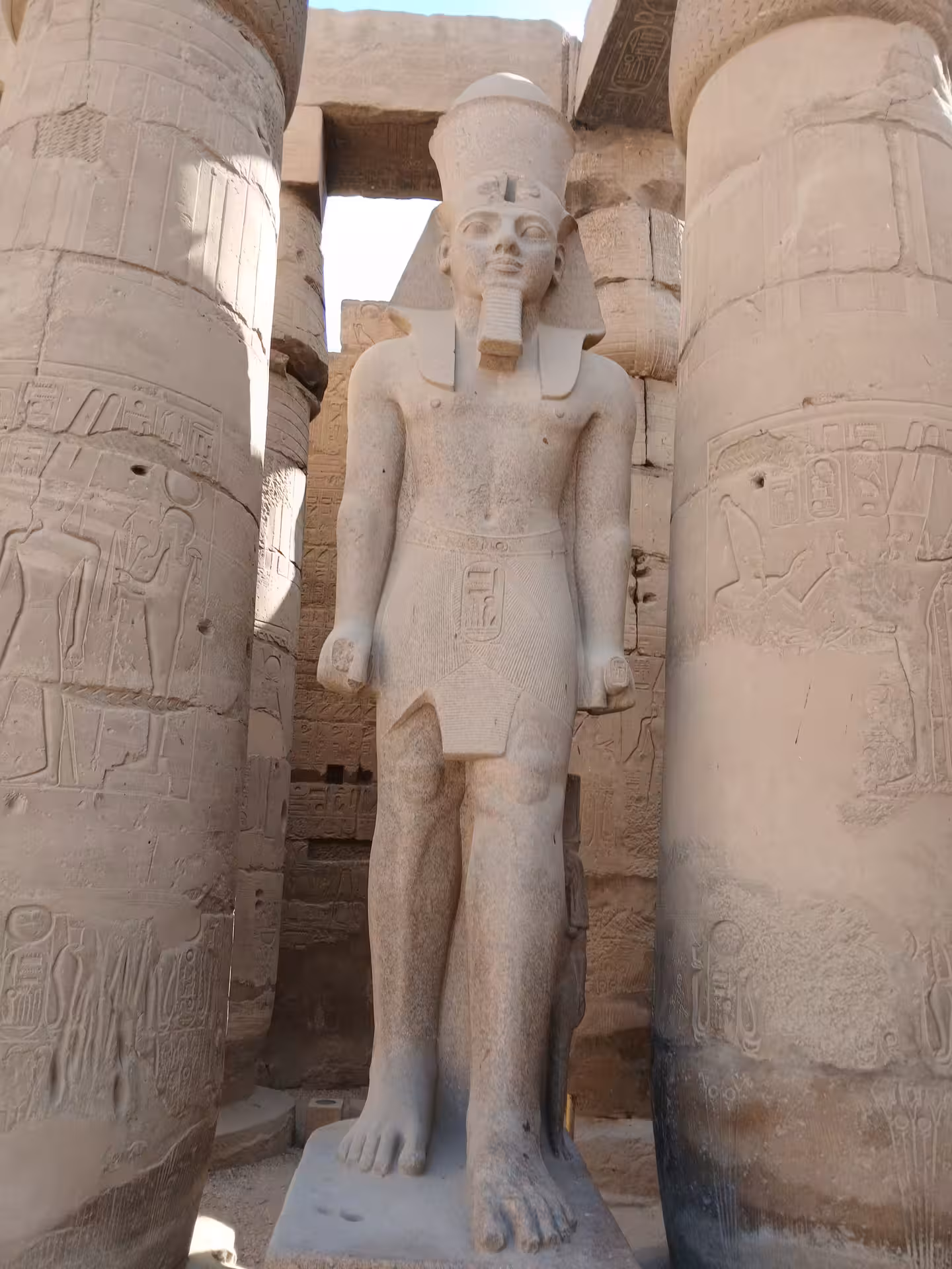 Statue of ancient Egyptian pharaoh among hieroglyph-covered columns in Luxor temple, Egypt travel destination.