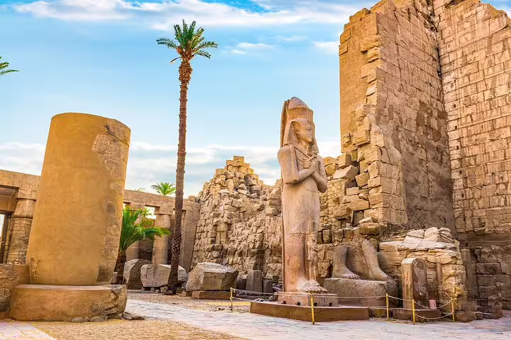 Luxor Temple ruins with pharaoh statue and palm tree, seen on a private Luxor day trip from Cairo by plane