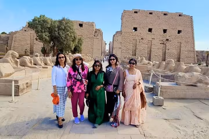 Group of tourists exploring ancient ruins at Luxor West Bank, surrounded by historic stone statues and structures.