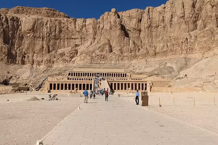 Visitors walking towards the majestic Mortuary Temple of Hatshepsut on Luxor West Bank tour.