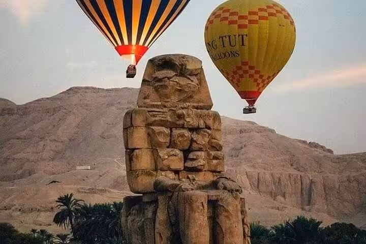 Majestic hot air balloons soar above the ancient Colossi of Memnon in Luxor's West Bank, Egypt.