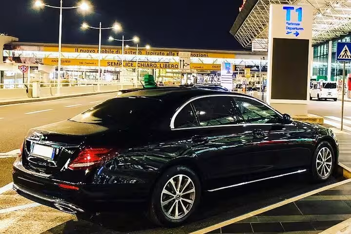 Luxury black car parked outside Terminal 1 at Fiumicino Airport, ready for airport transfer services.