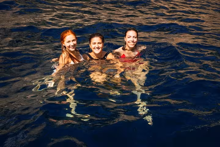 Three women enjoying a swim in the crystal-clear waters during a luxury boat tour off the Amalfi Coast.
