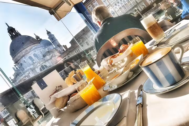 Luxurious breakfast setup with fresh juices and coffee, overlooking a stunning Venetian landmark in the morning light.