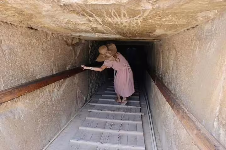 Visitor descending a narrow ancient passage inside an Egyptian tomb on the luxury 8-day Cairo and Oberoi Philae Nile cruise