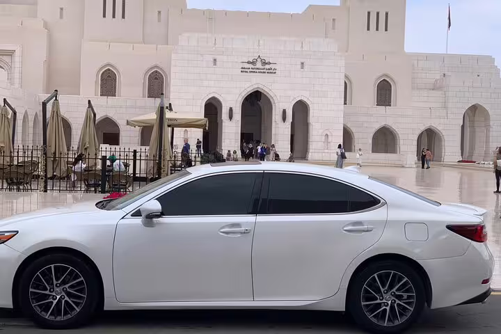 Luxury car parked in front of Muscat's iconic architecture, offering a premium private driver experience.