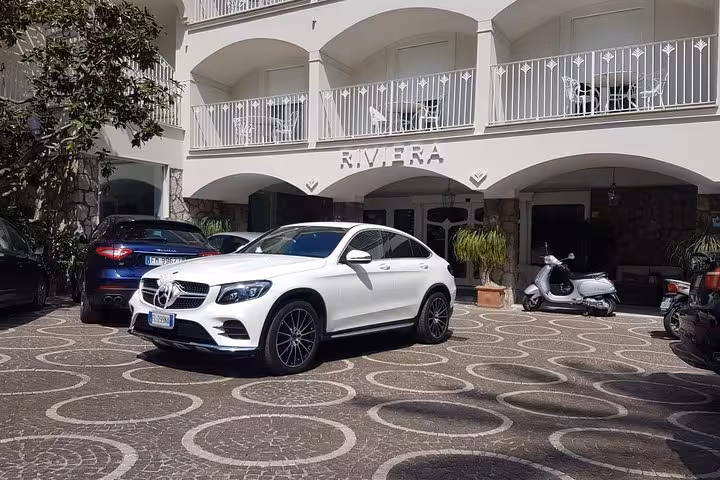 White luxury car parked at a hotel entrance, symbolizing comfort and style for private transfers to Sorrento.