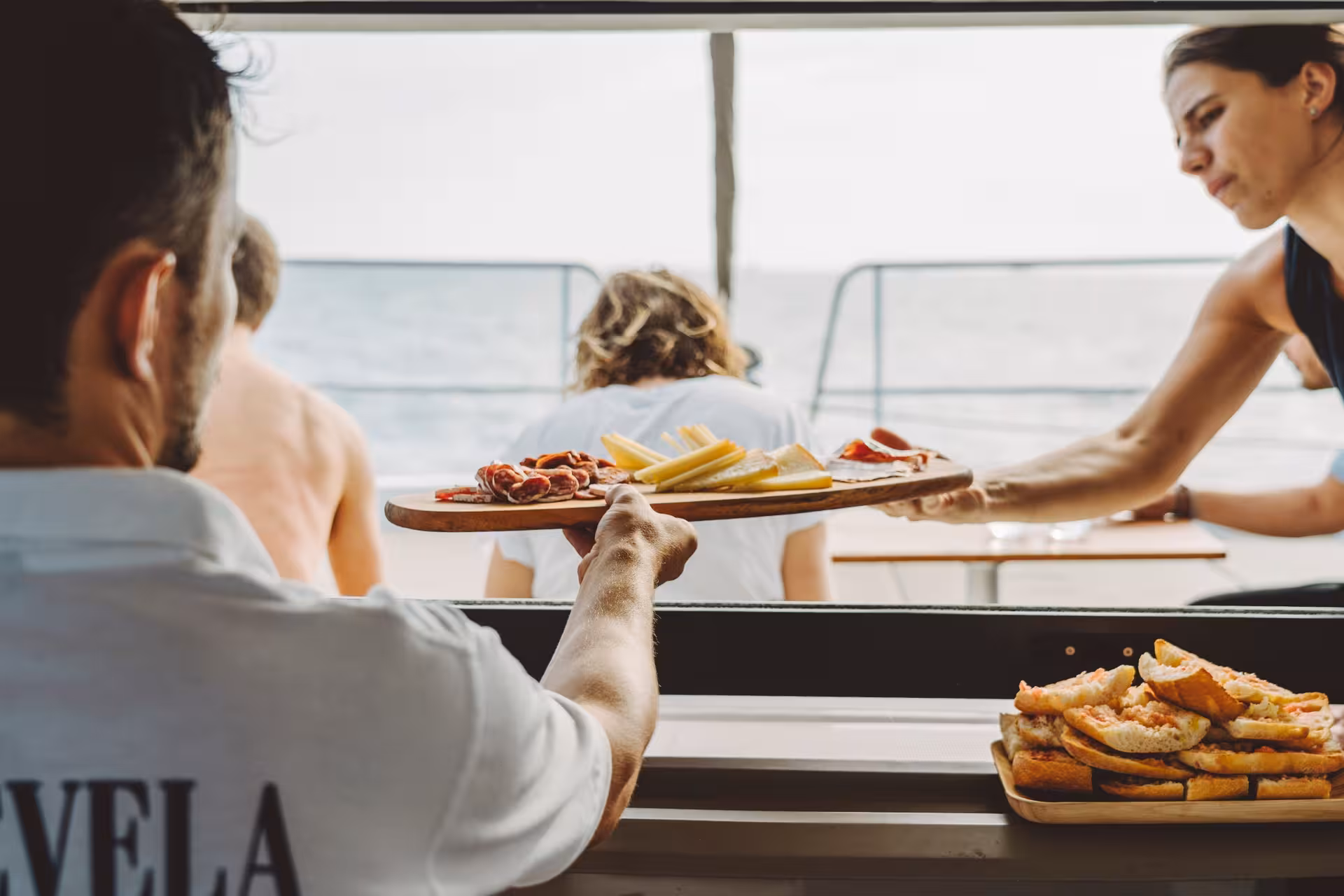 Crew serving tapas and cheese platter onboard private Bali 4.1 luxury catamaran tour along Barcelona coast