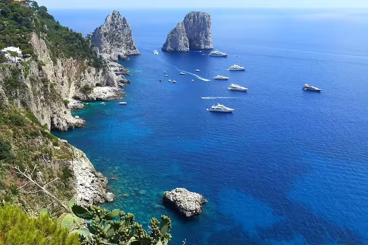 Luxury yachts anchored by Capri’s Faraglioni cliffs in crystal-clear Tyrrhenian Sea on a weekly catamaran cruise