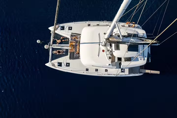 Aerial view of a luxurious catamaran sailing in deep blue waters of Santorini, ideal for a half-day cruise adventure.
