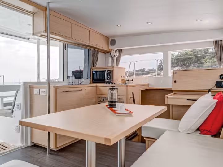 Modern catamaran interior with a cozy dining area, sunlight streaming through large windows, ideal for relaxation.