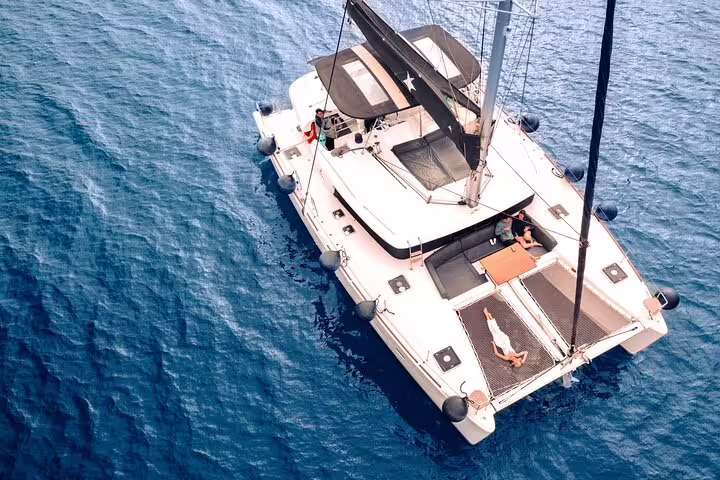 Aerial view of luxury catamaran cruising the azure waters of Santorini on a premium half-day tour.