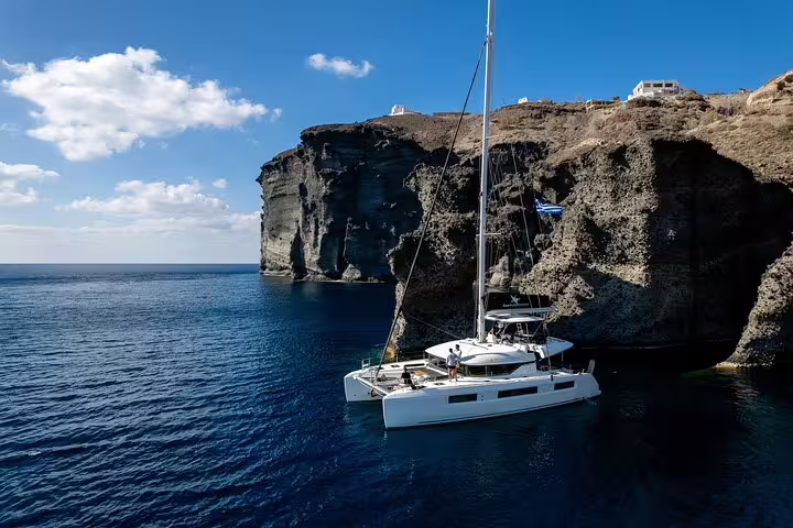 Luxury catamaran anchored near Santorini's dramatic cliffs under a clear blue sky on an exclusive half-day cruise.