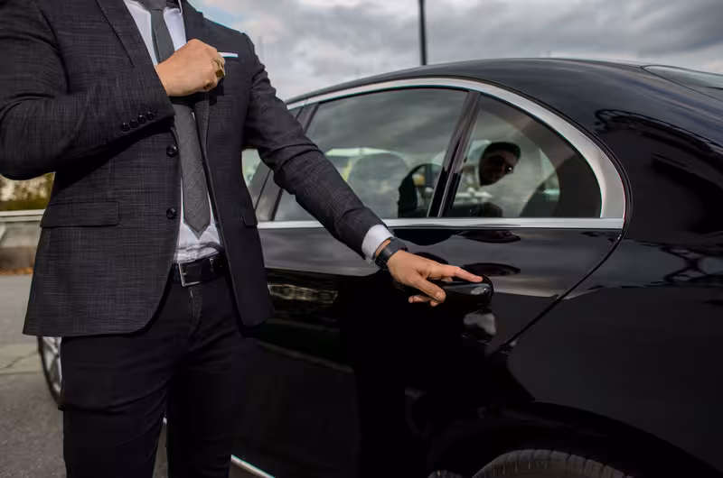 Chauffeur in a suit opening the door of a luxury car for a private transfer from Lisbon Airport to hotel.