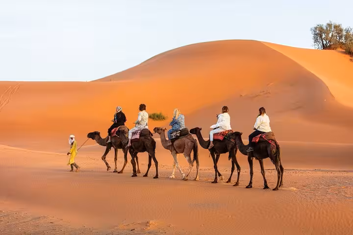 Tourists on camels traverse the golden dunes of Merzouga, highlighting a luxury desert tour from Fes to Marrakech.