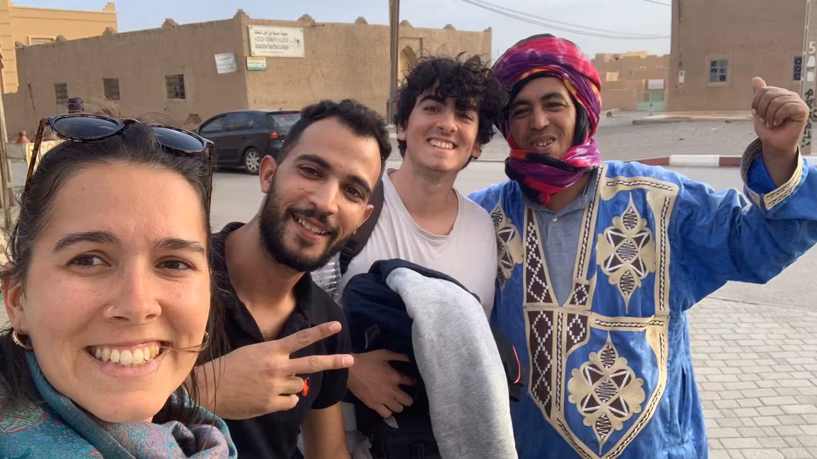 Tourists smiling with local guide in traditional attire during luxury desert tour from Errachidia to Fes via Merzouga.