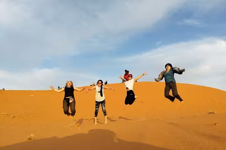 Group jumping on golden Sahara dunes during 2-day luxury desert tour from Fes to Marrakech adventure.